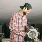 Person in plaid shirt and ear protection using a circular saw in a workshop