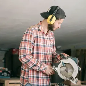 Person in plaid shirt and ear protection using a circular saw in a workshop