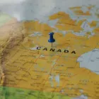 Blue pushpin marking Canada on a yellow map of North America.