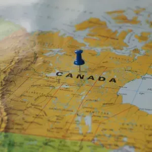 Blue pushpin marking Canada on a yellow map of North America.