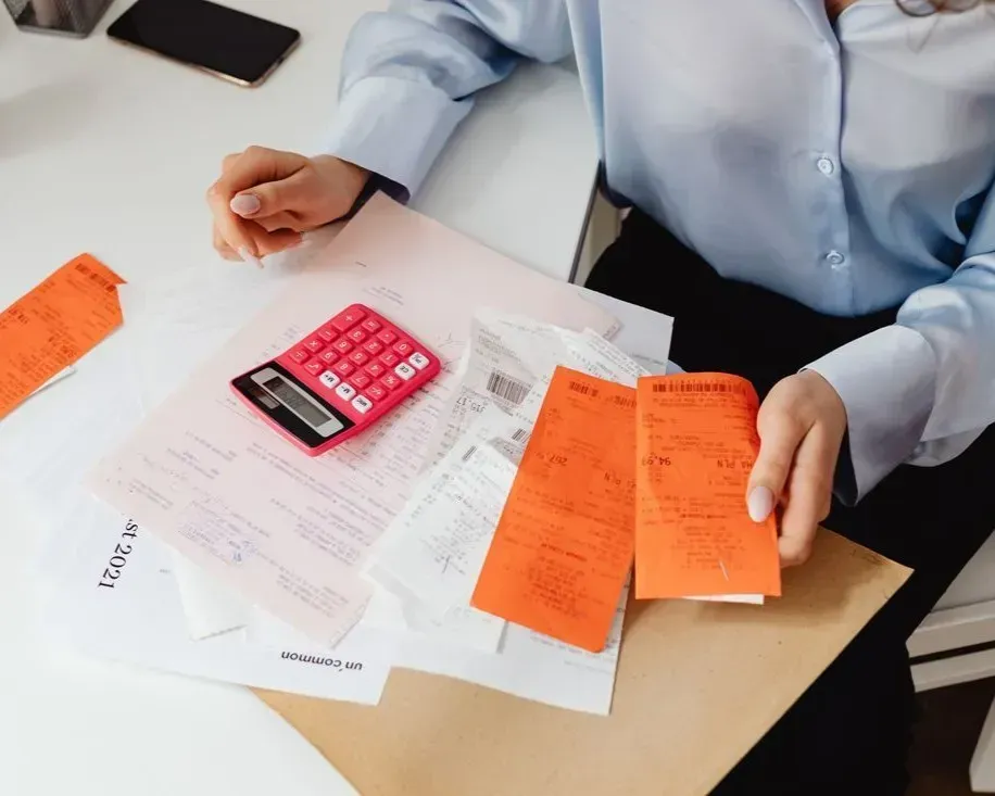 Person at desk with pink calculator, papers, and orange receipts reviewing finances