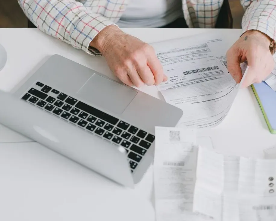 Hands reviewing documents beside a silver laptop on a white desk