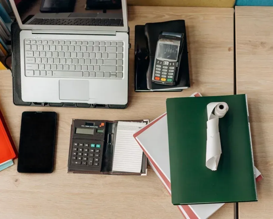 Desk with laptop, calculator, phone, notebook, and green binder with a white handle