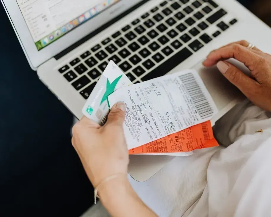 Hands holding receipts over a laptop keyboard with a calculator, reviewing expenses.