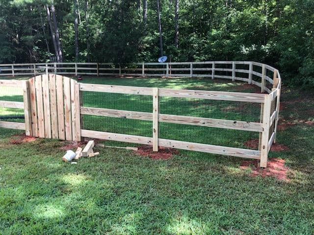 Wooden fenced pen in a grassy yard beside a road and trees