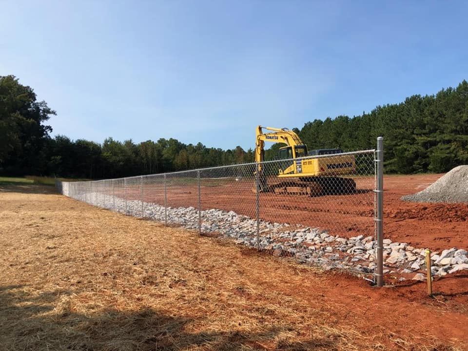 Yellow excavator on a fenced construction site with dirt and gravel piles under a blue sky