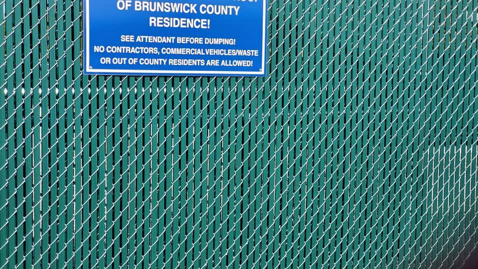 Blue sign on chain-link fence reading “Brunswick County Residence” with smaller no-trespassing text.