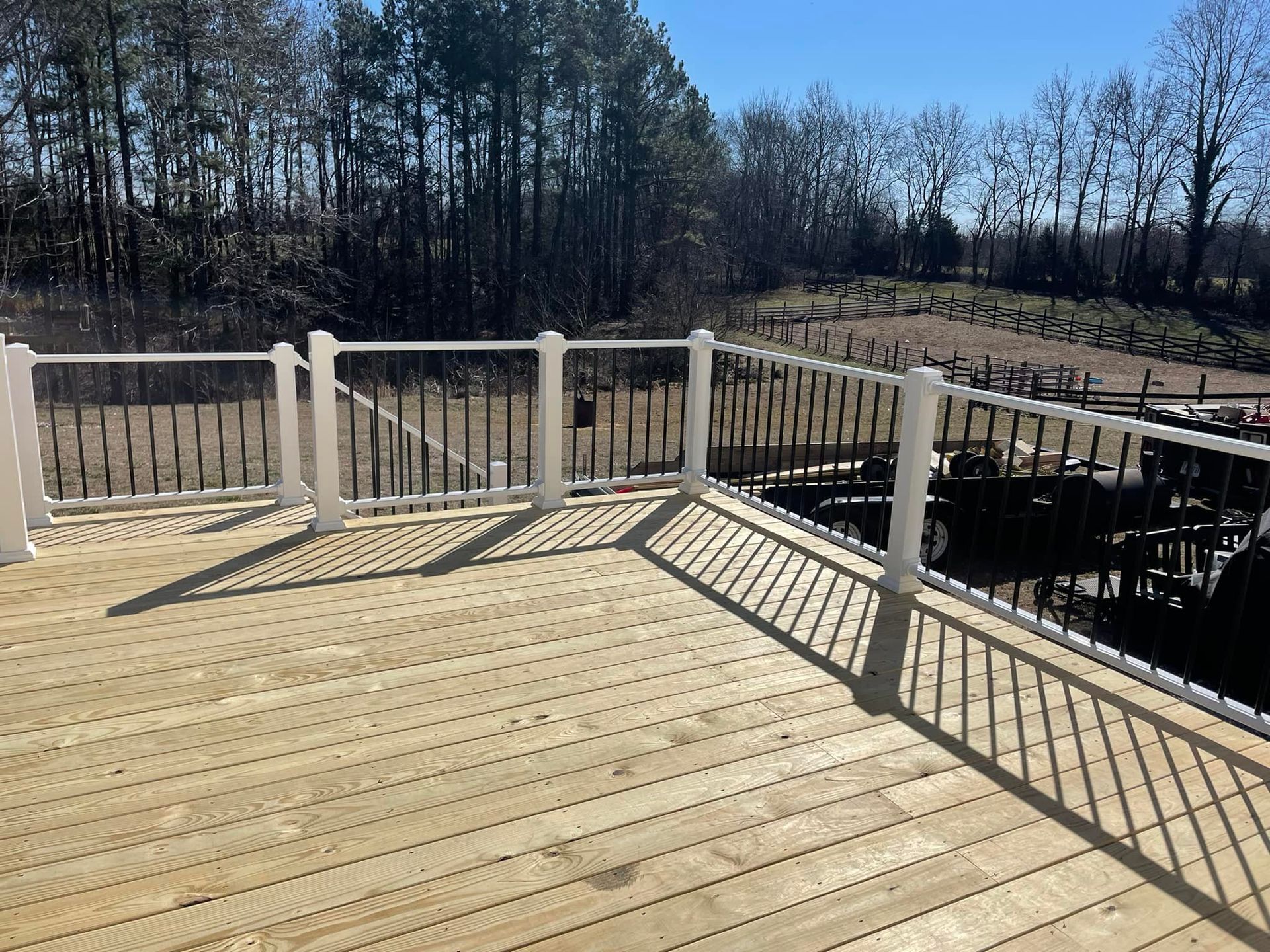 Wooden deck with white railings overlooking a wooded backyard in daylight