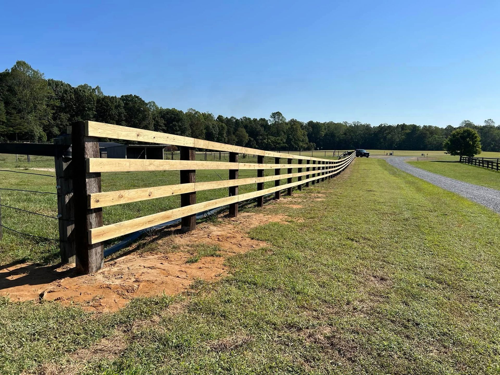 Wooden fence along a grassy field beside a curving gravel path under a clear blue sky
