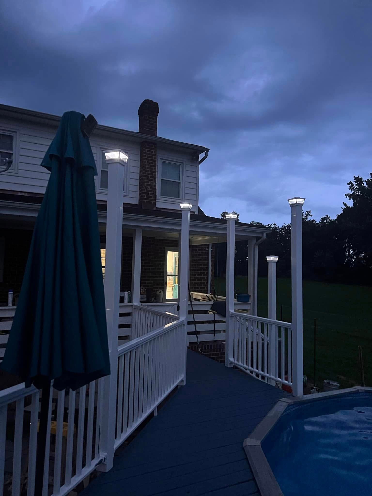 Twilight view of a house deck and walkway with white railings and a closed patio umbrella.