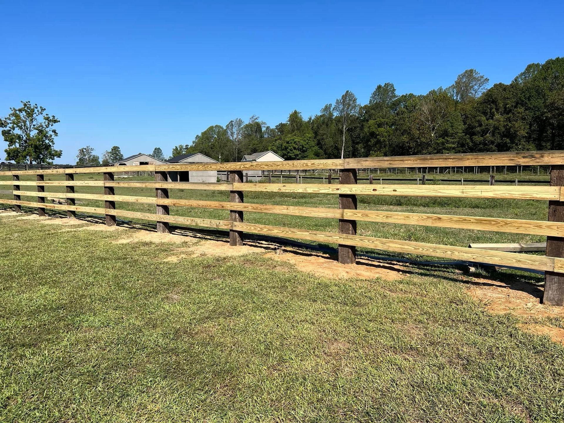 Wooden fence along a grassy field under a clear blue sky.