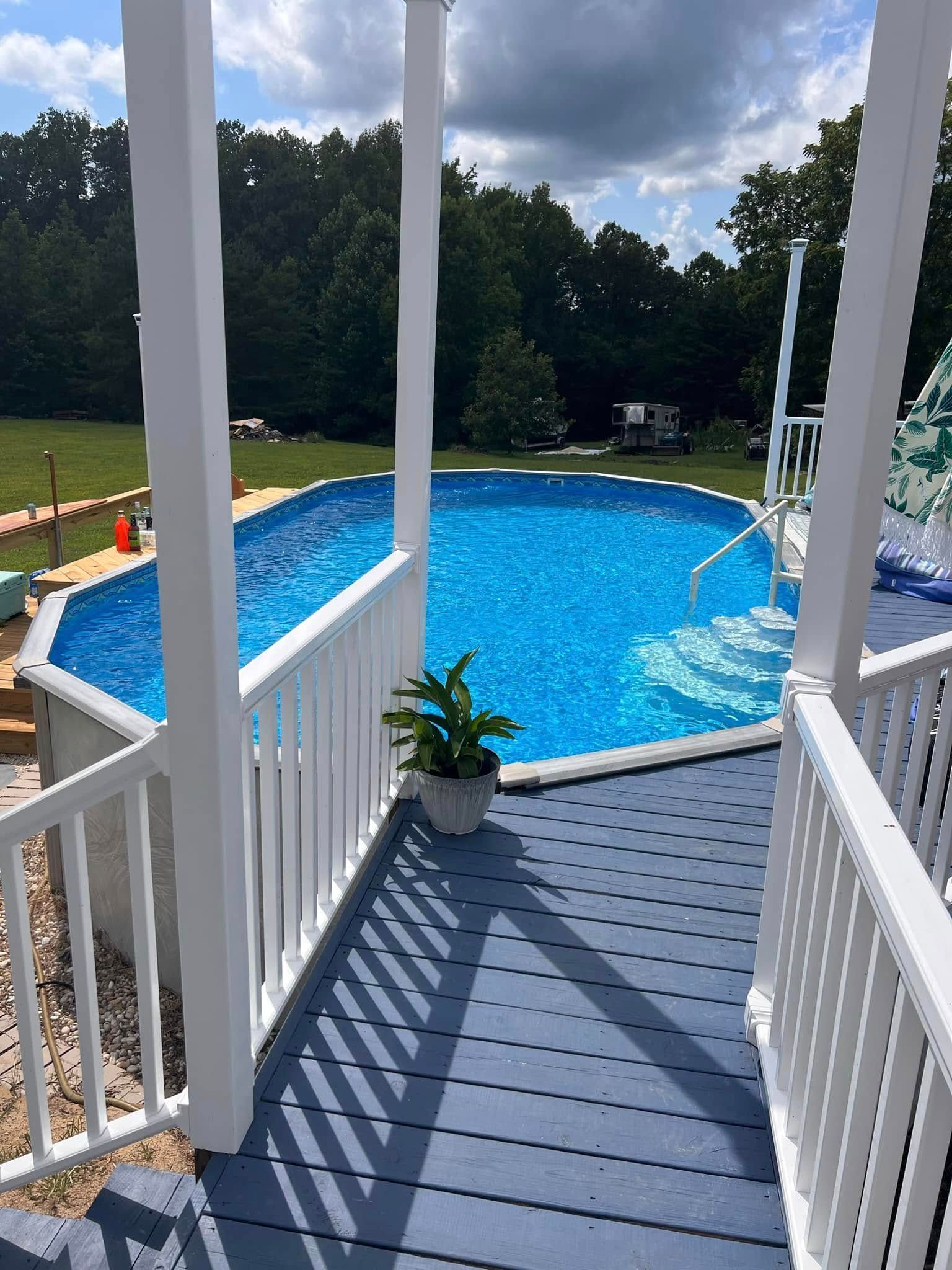 White porch steps leading to a bright blue backyard pool beside a green lawn and trees
