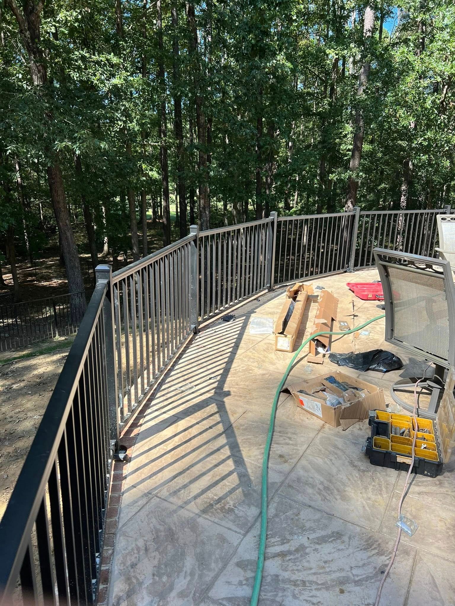 Curved black metal railing around a deck under construction in a wooded backyard.
