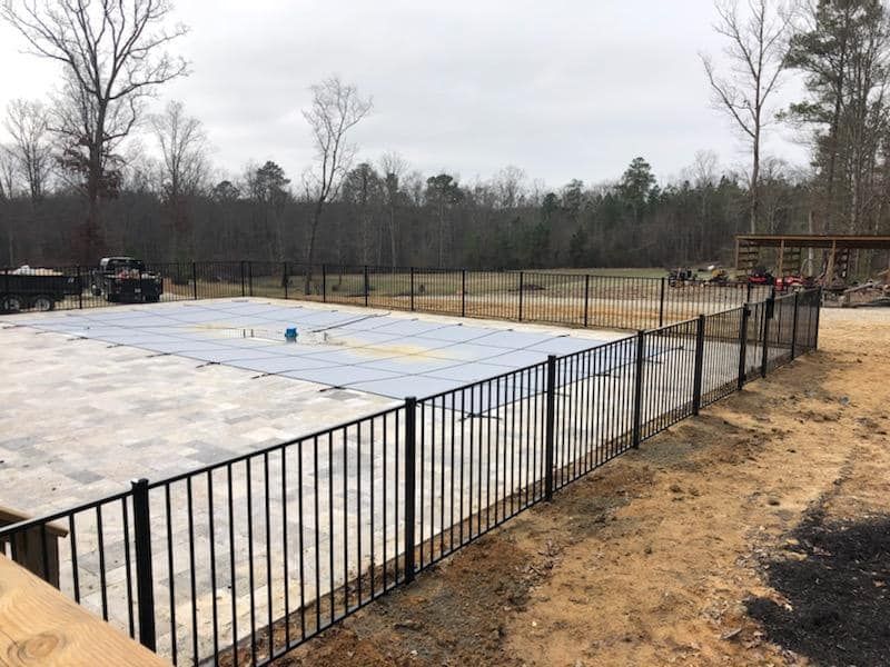 Empty fenced pool area with a covered white surface in a wooded yard