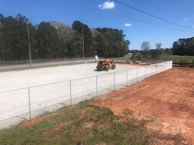 Bulldozer grading a dirt lot beside a chain-link fence under a blue sky