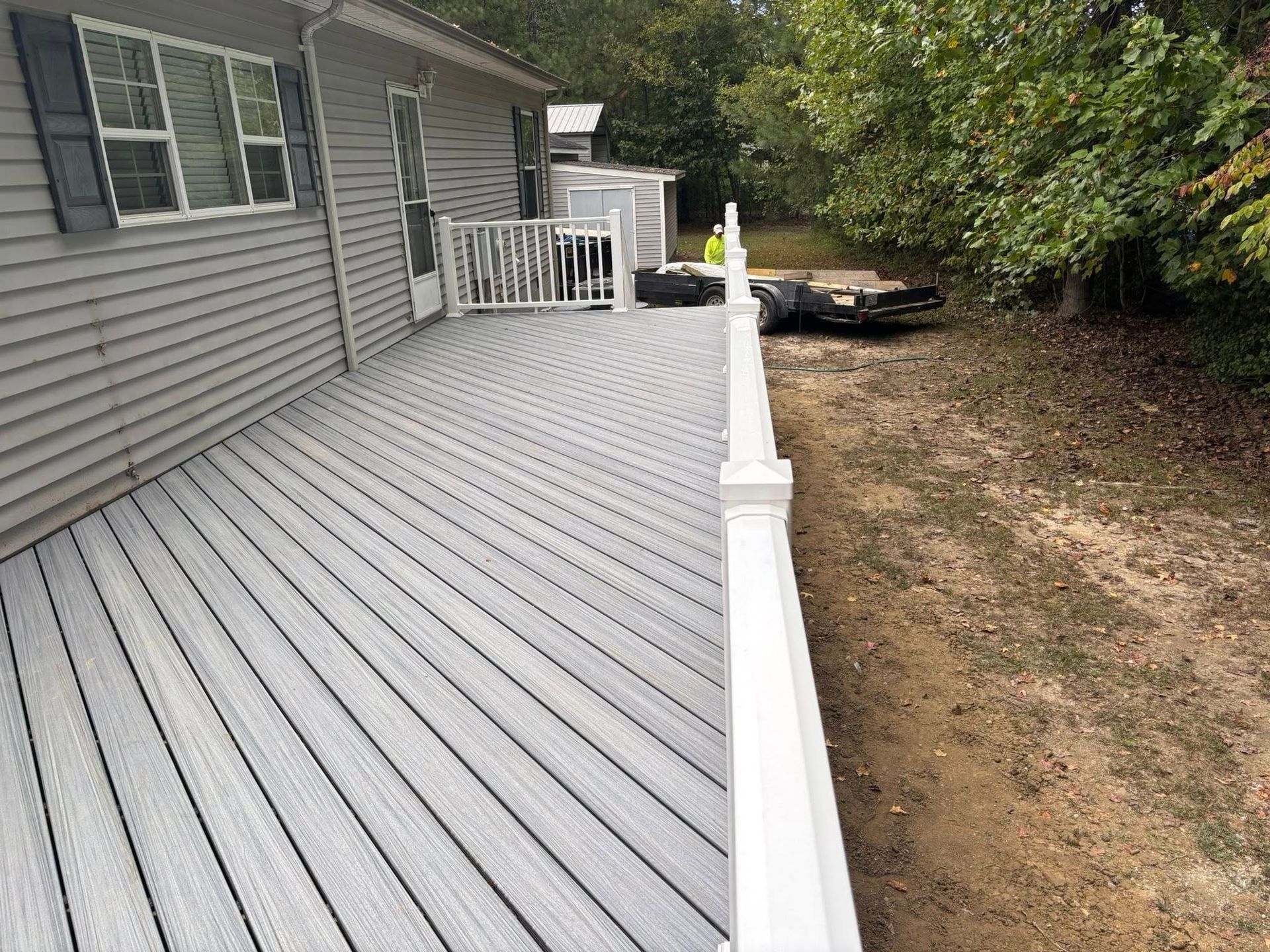 Gray house deck with white railing and steps, extending along a backyard beside grass and trees