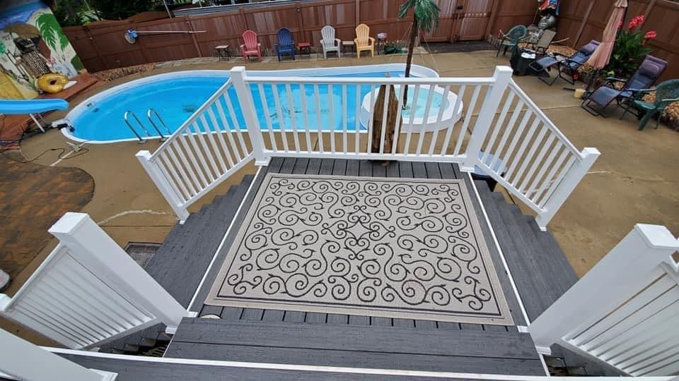 Back deck with white railings and patterned rug overlooking a backyard pool and patio chairs