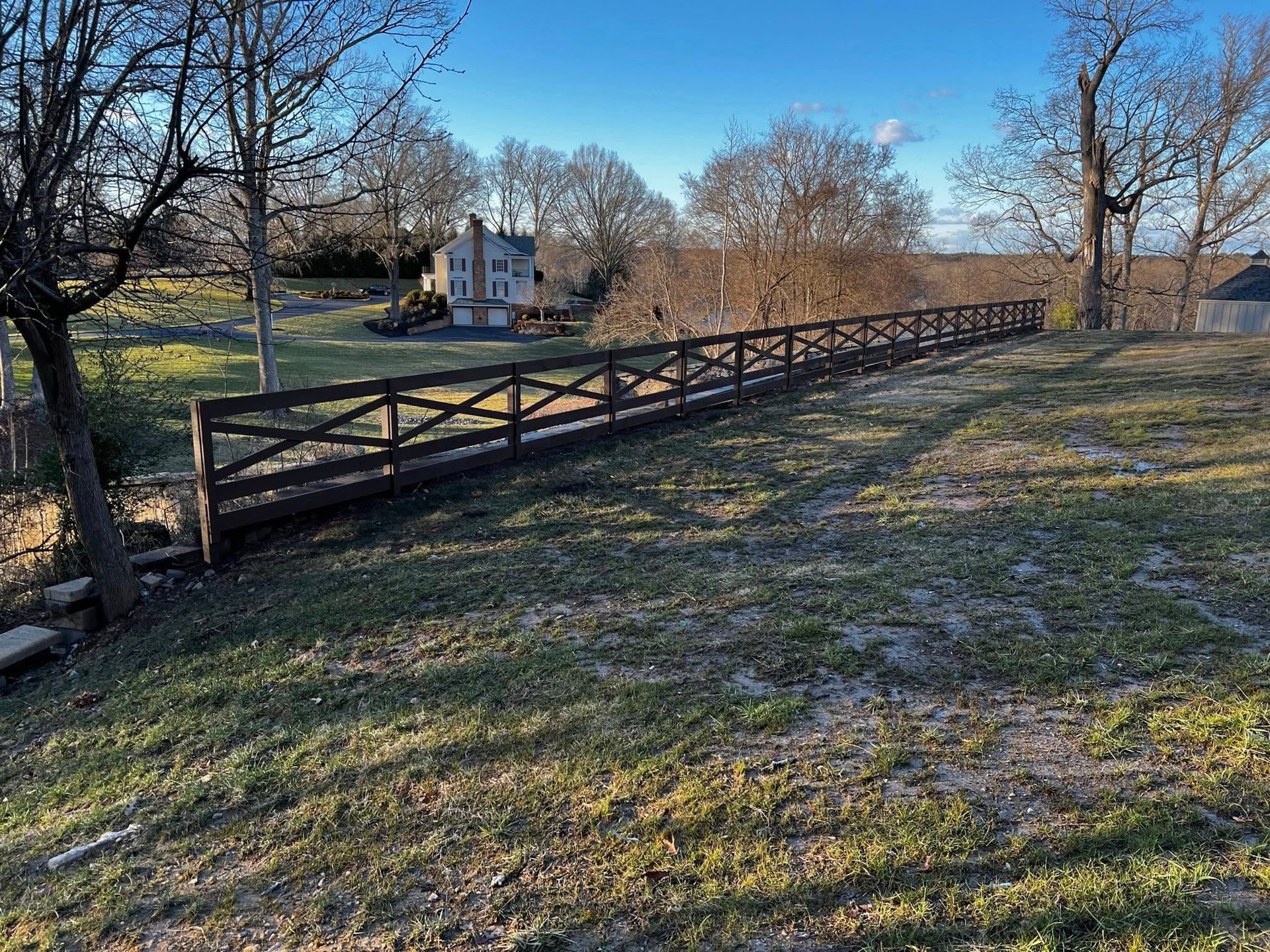 Wooden fence beside a grassy yard with bare trees under a clear blue sky