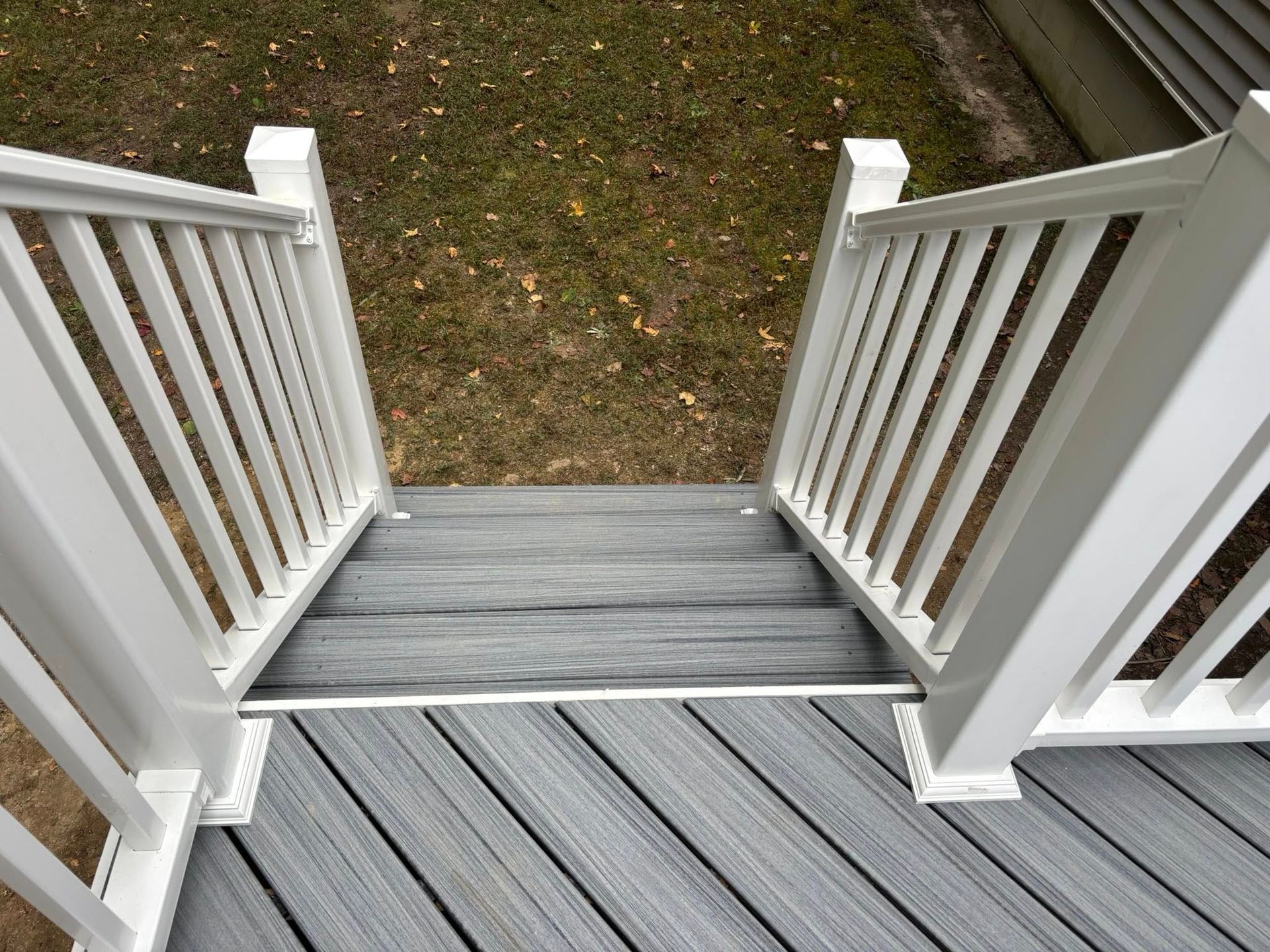 Wooden front porch steps with white railings leading down to a grassy yard