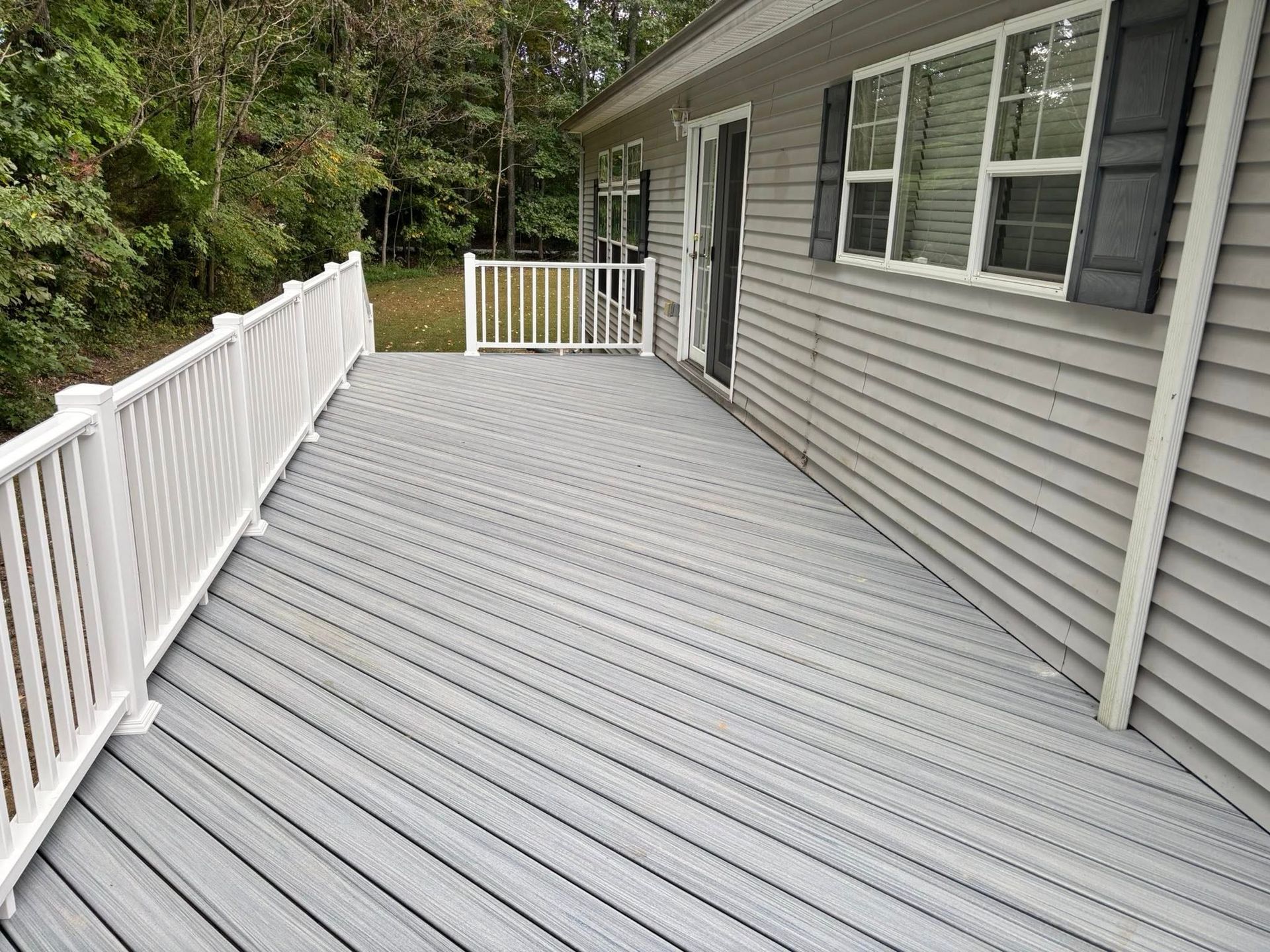 Gray deck with white railing beside a house and wooded backyard
