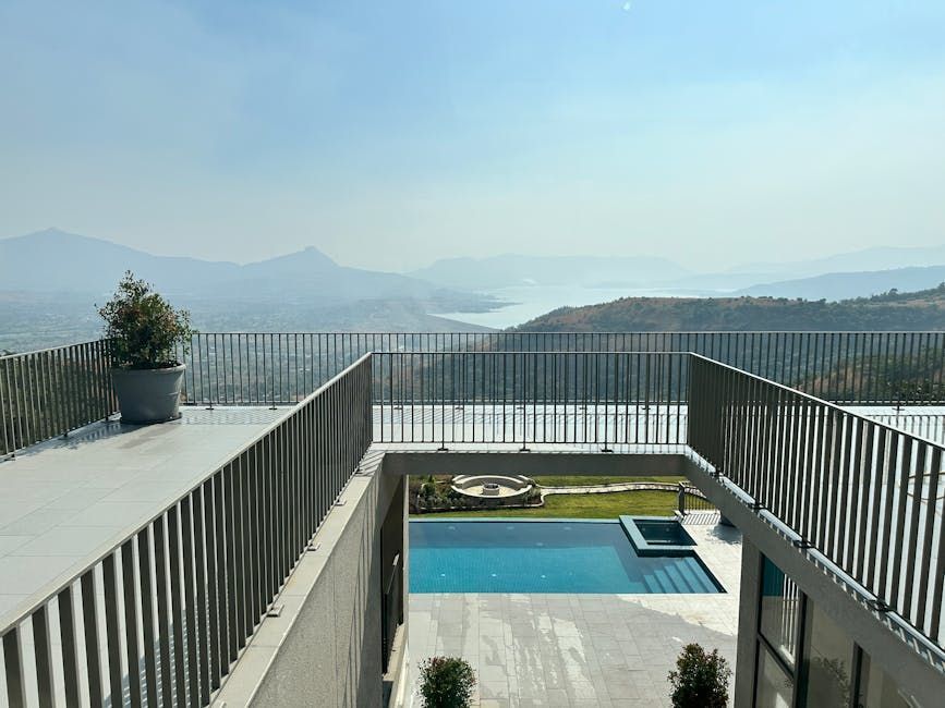 Modern balcony overlooking a blue pool, mountains, and a hazy lake under a clear sky