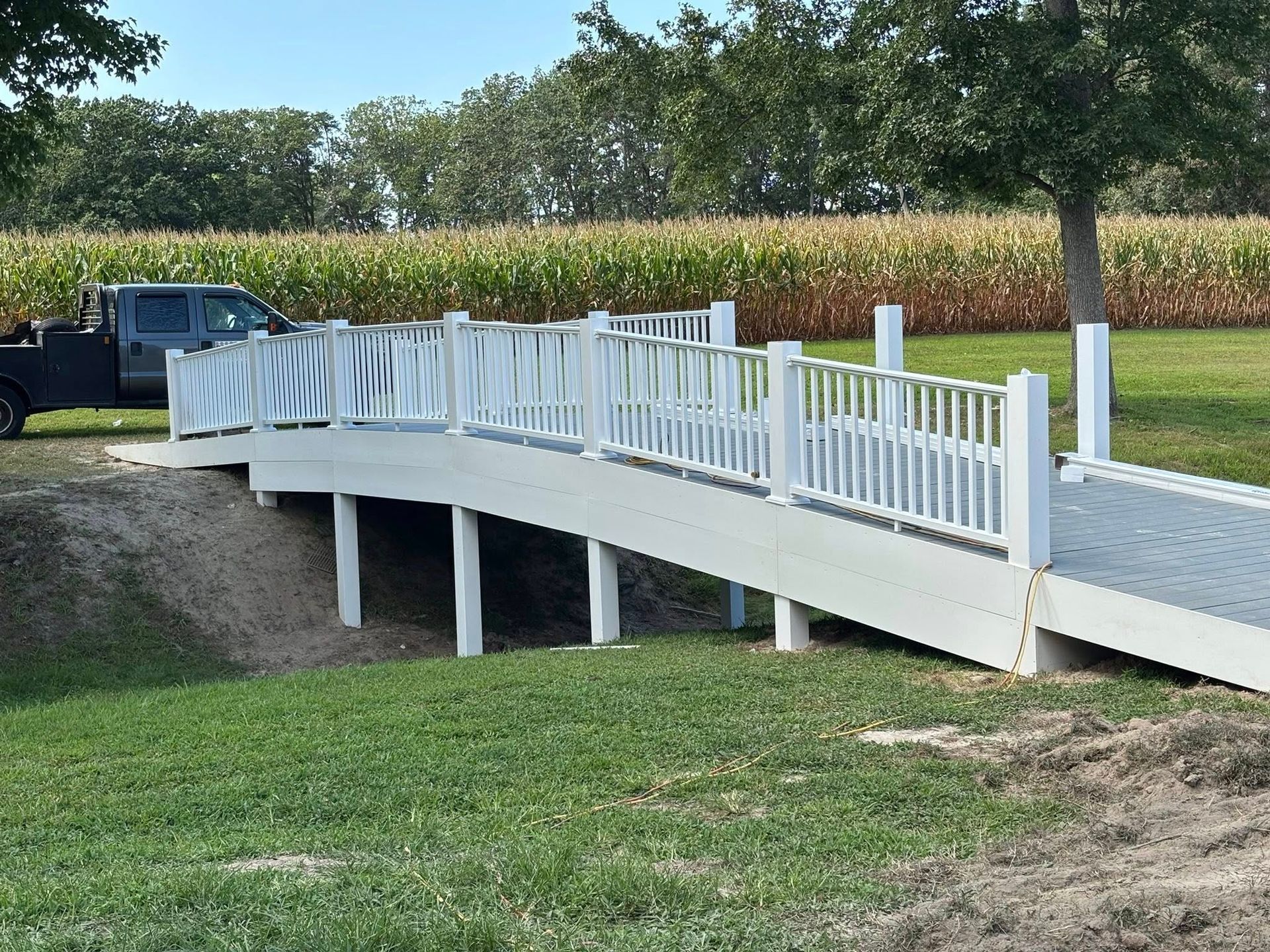 White-railed concrete bridge over a grassy ditch beside a cornfield and parked truck