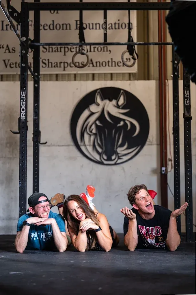 Three performers lying onstage beneath a hanging circular logo, with a black backdrop and red accents.