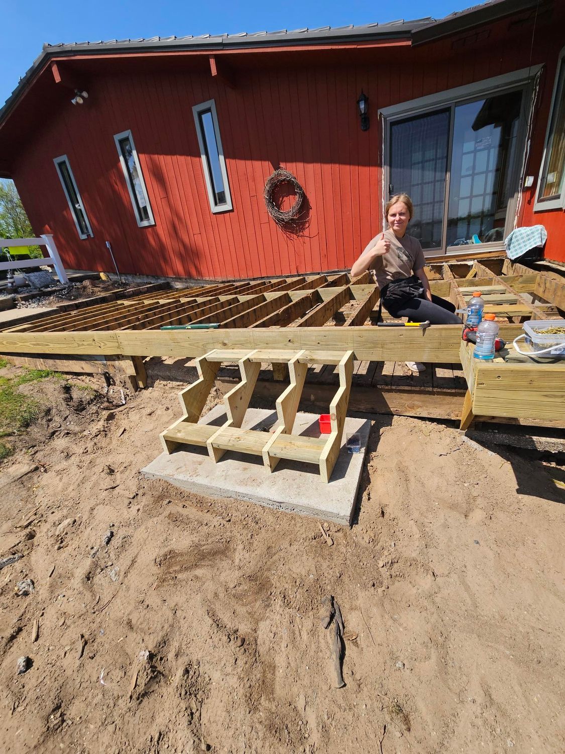 Person on a wooden ramp under construction beside a red house, with tools and building materials nearby