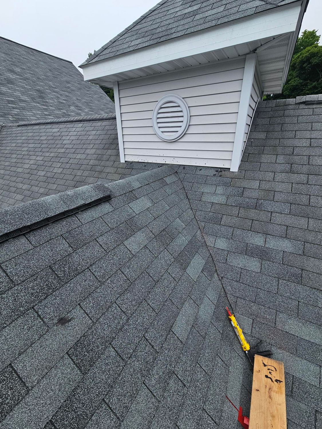 Roof shingles around a vent with a roofing tool in the foreground