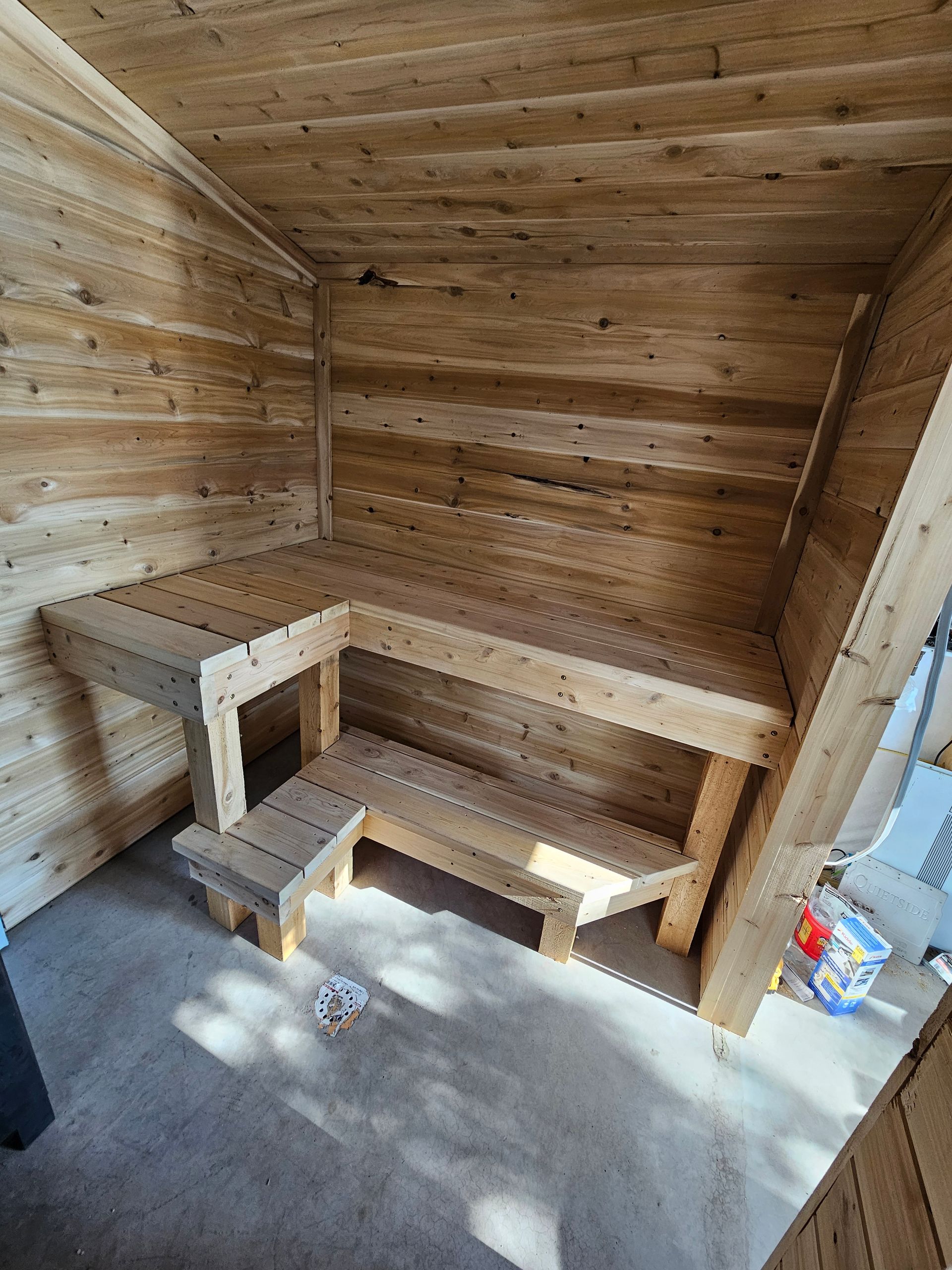 Wood-paneled sauna with tiered benches and a small step stool on a concrete floor