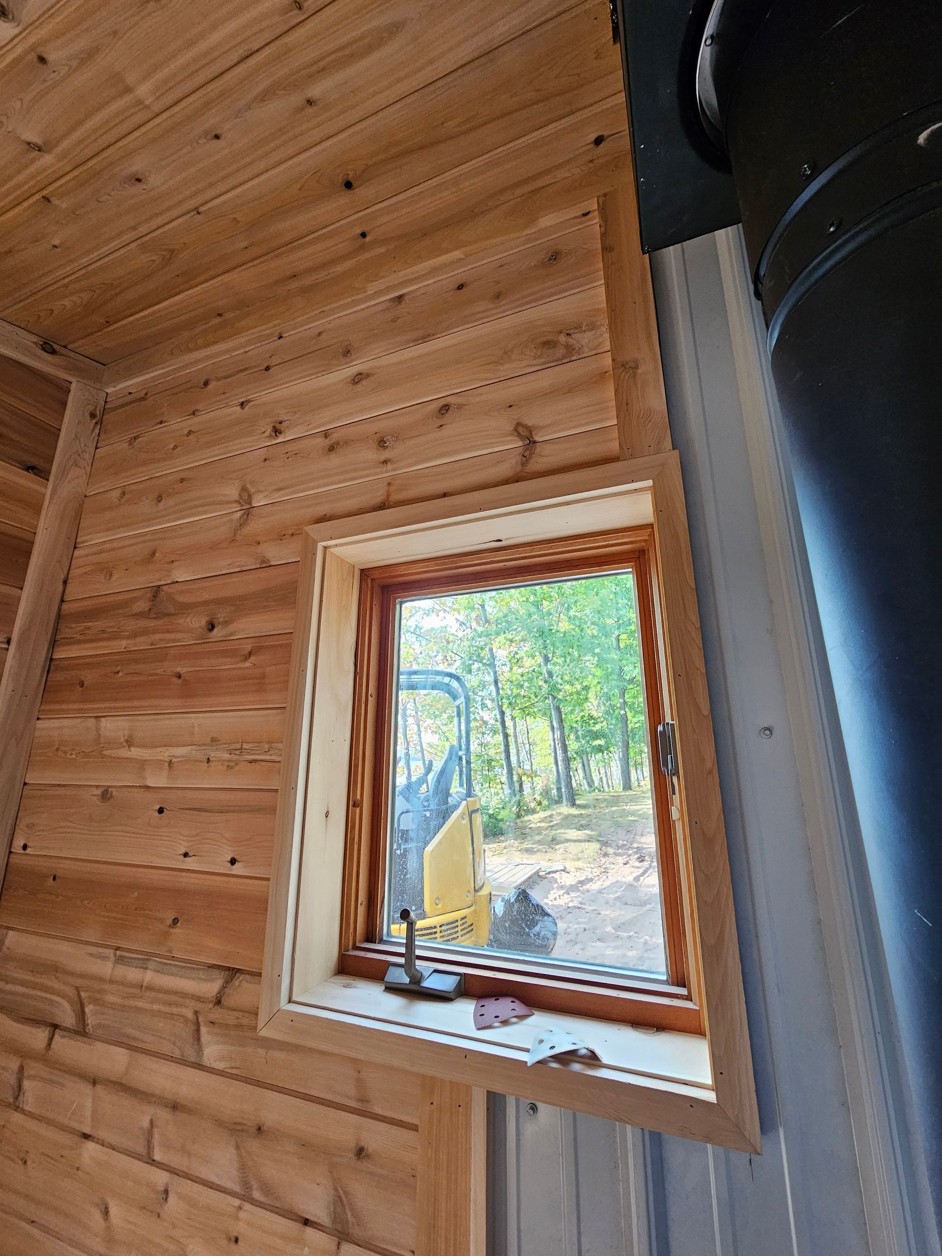 Wood-paneled cabin wall with a small window overlooking trees and outdoor equipment.
