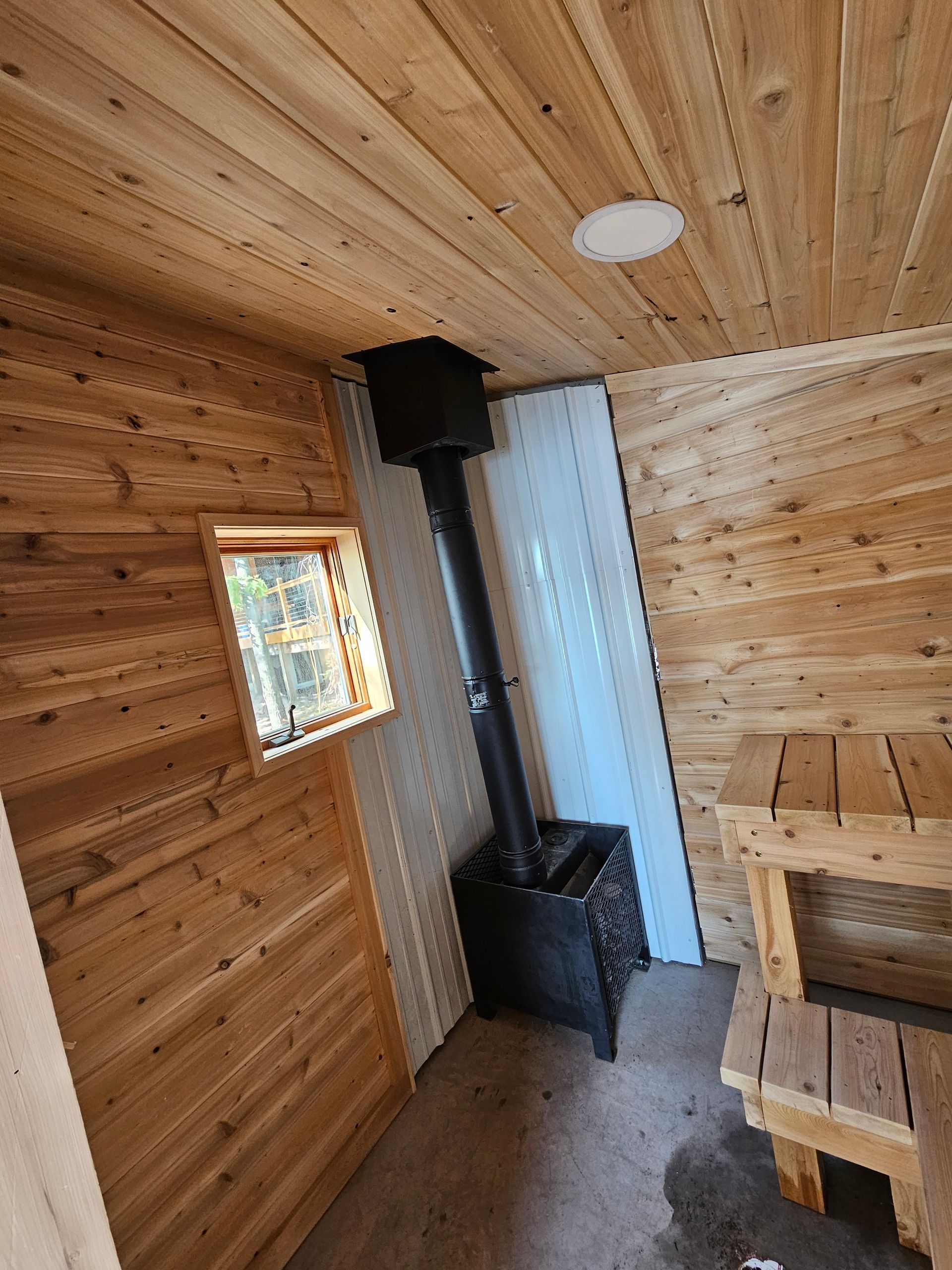 Small wood-paneled room with a black wood stove, window, and built-in bench.