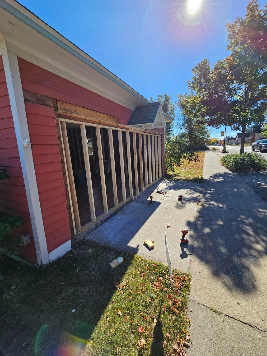 Red house exterior with damaged porch railing, sidewalk, and bright sunny street view