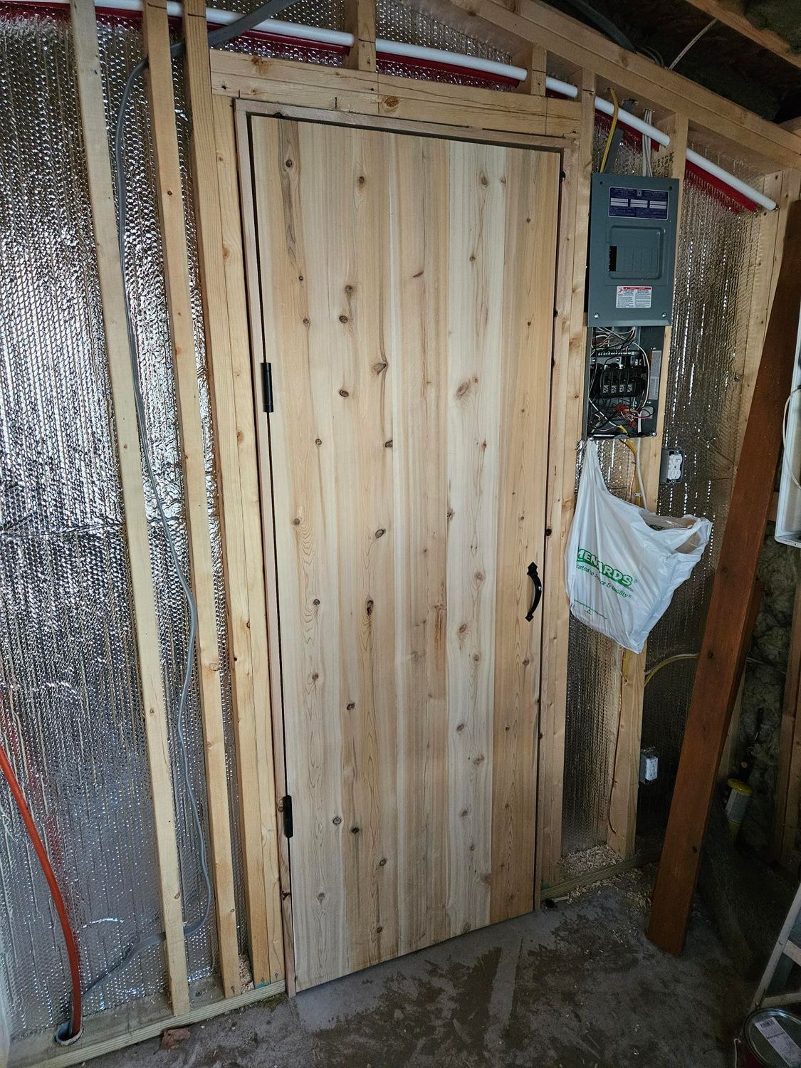 Wooden door framed by insulated walls, with electrical panel and construction materials nearby