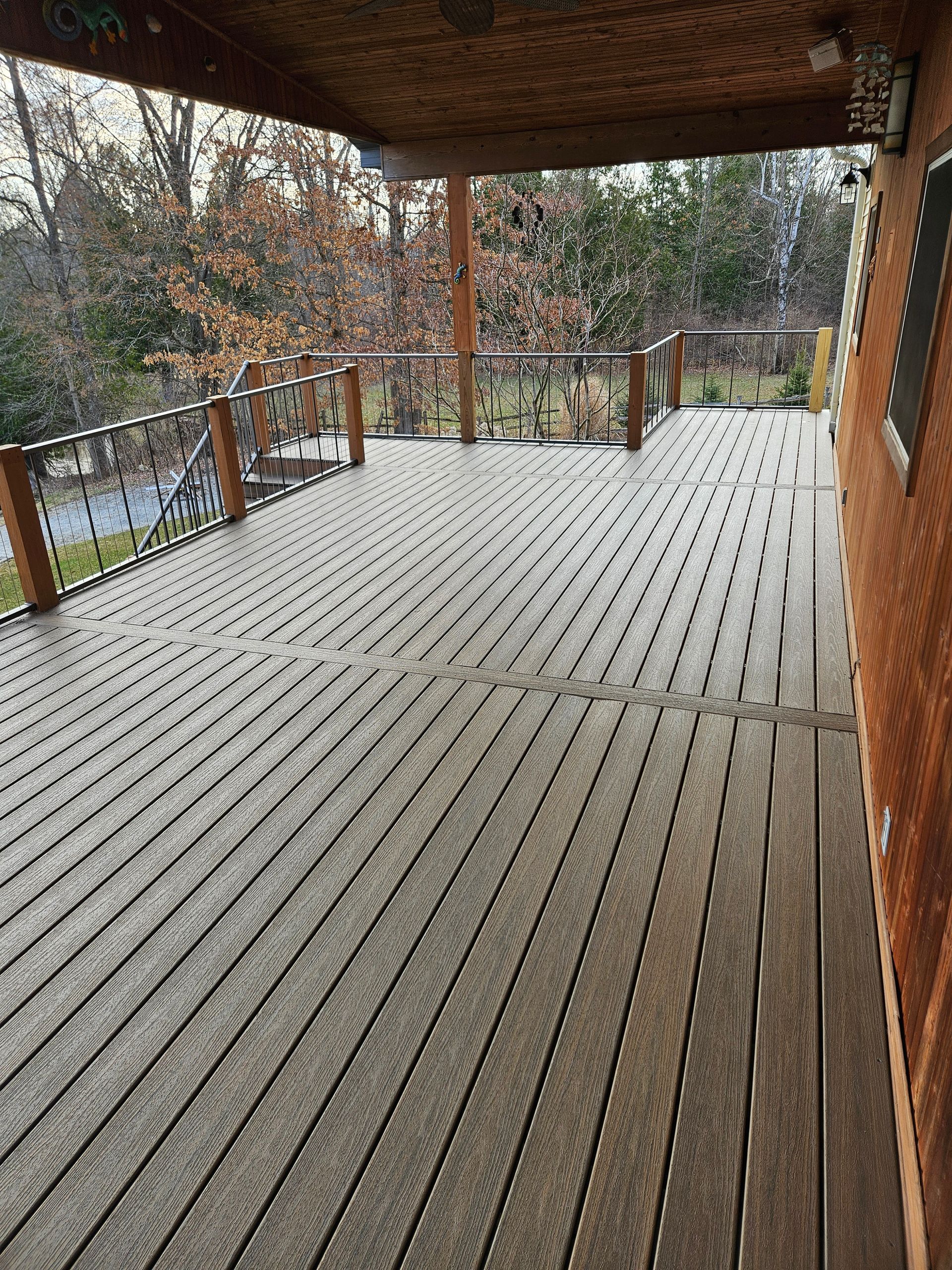 Covered wooden deck with wet boards, railing, and trees in the background