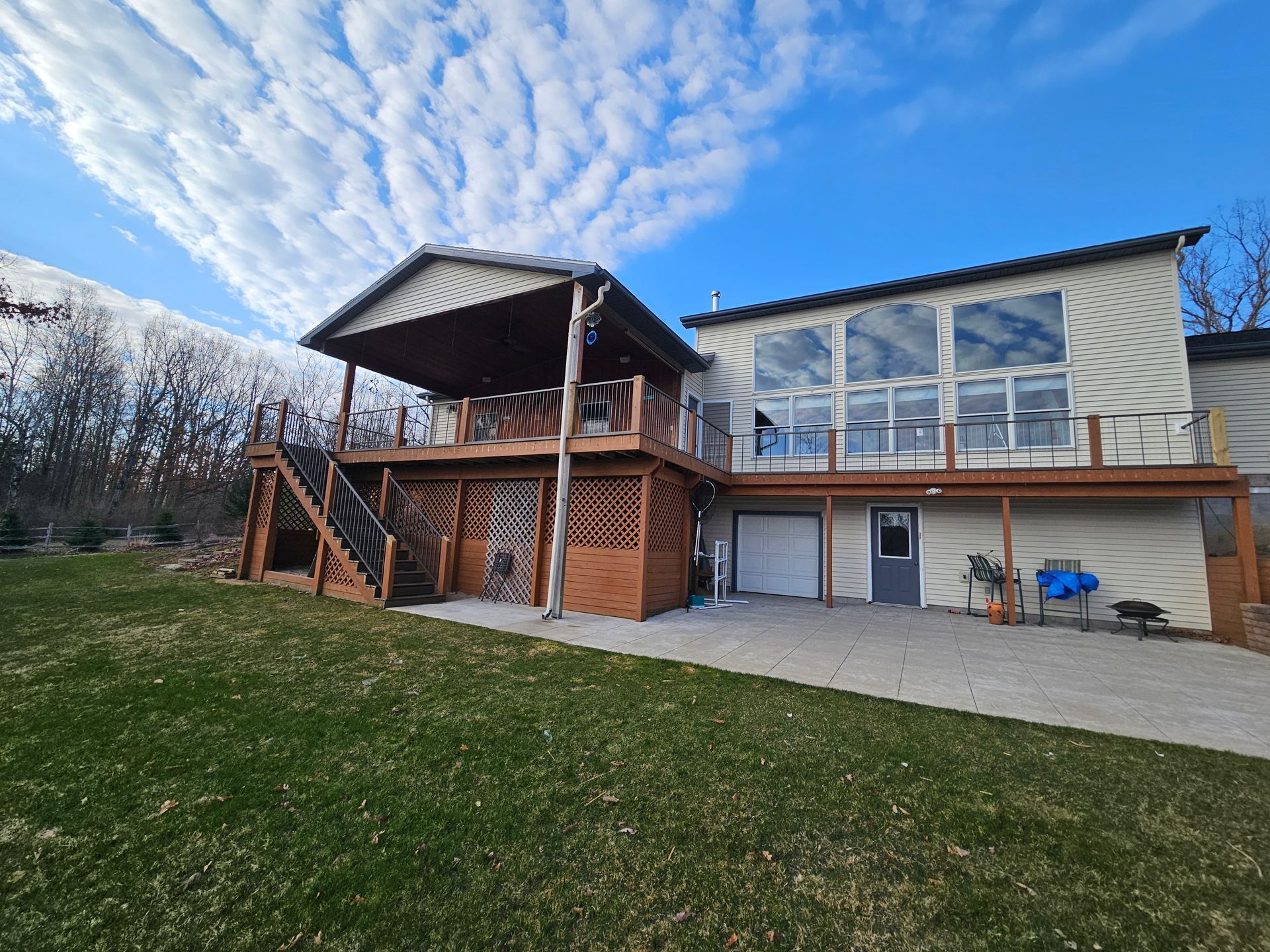 Modern two-story house with deck and stairway, under a blue sky on a grassy lawn