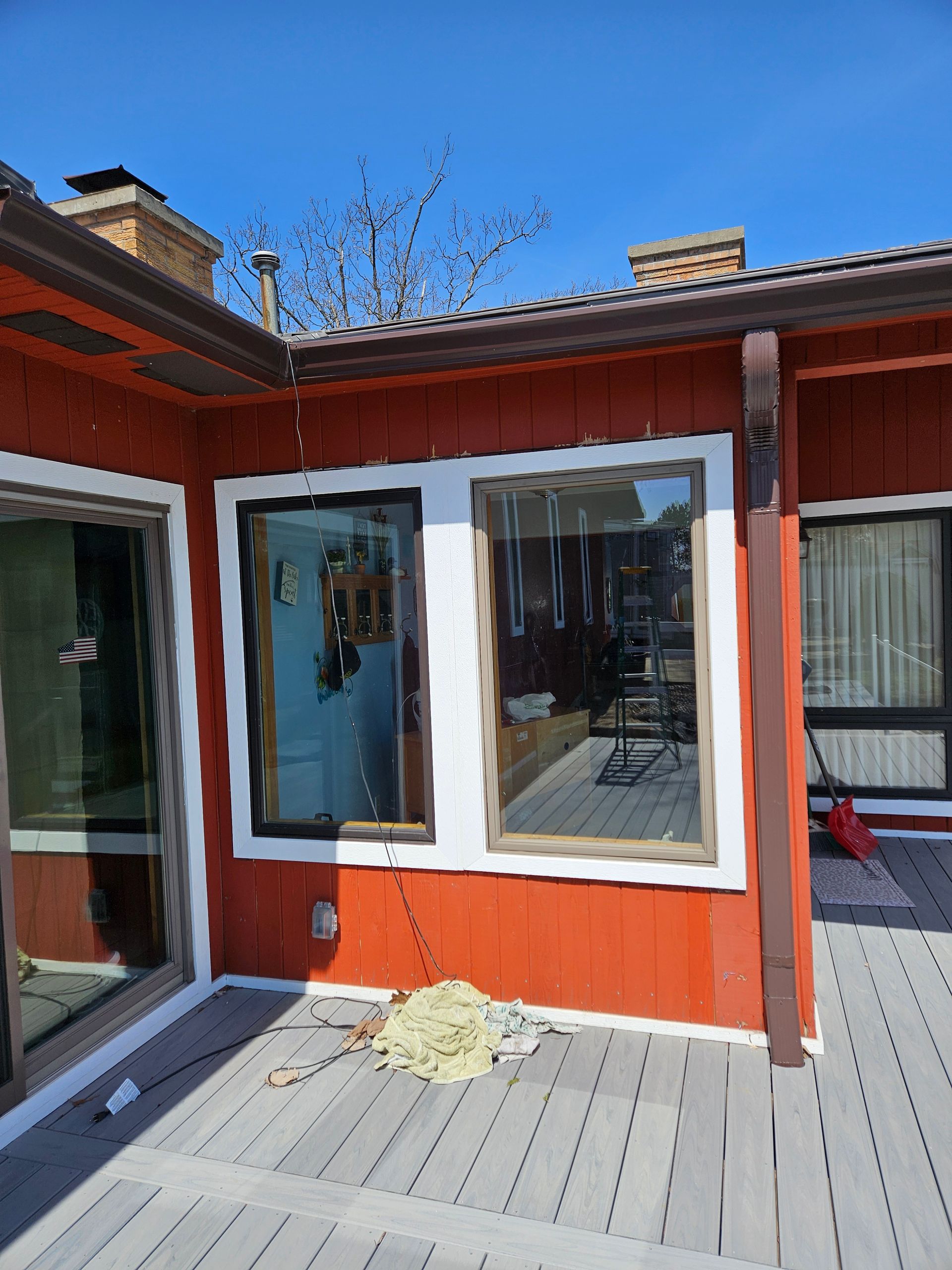 Red house exterior with white-trimmed windows and a gray deck in sunlight.