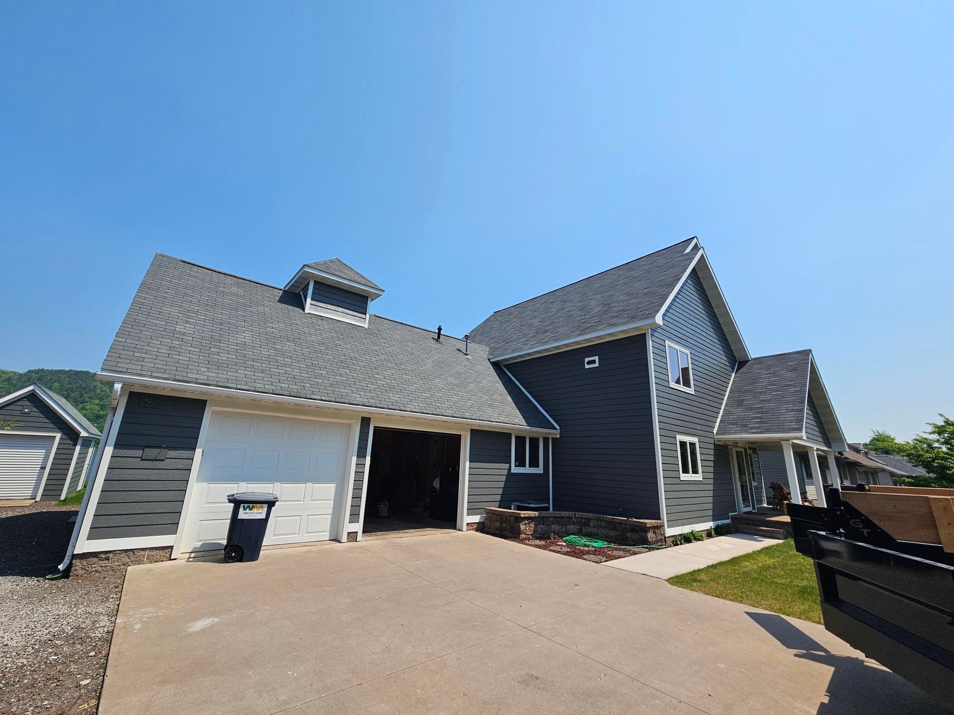 Suburban house with gray siding, attached garage, and wide driveway under a clear blue sky