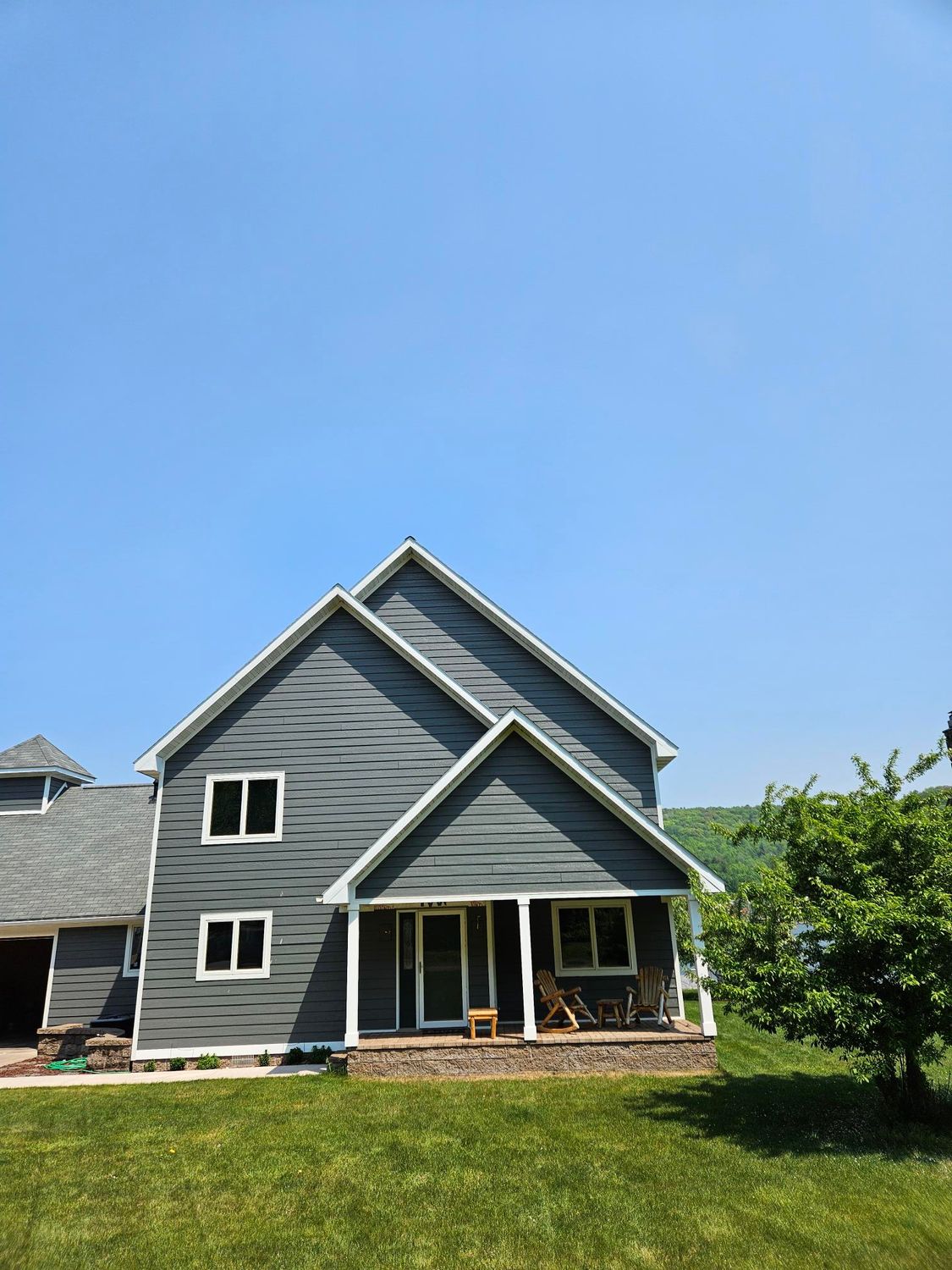 Gray house with white trim and porch on a green lawn under a clear blue sky