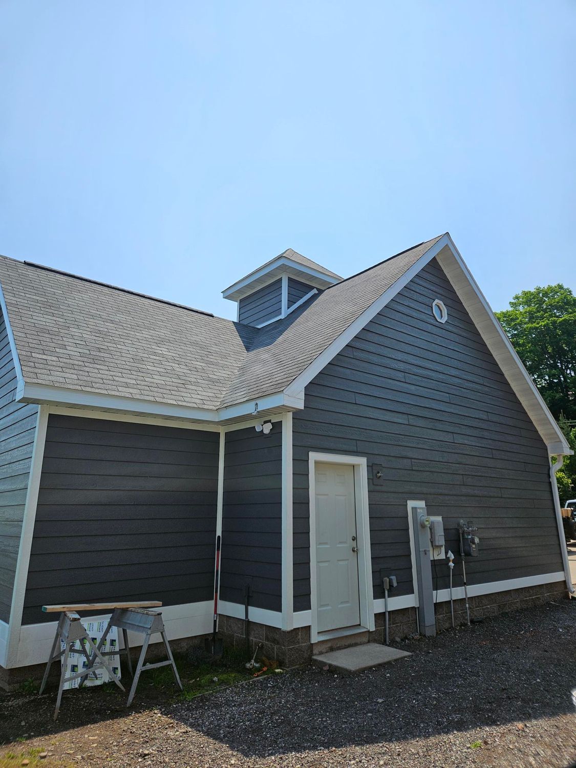 Dark gray house with white trim, steep roof, and small dormer under a blue sky.