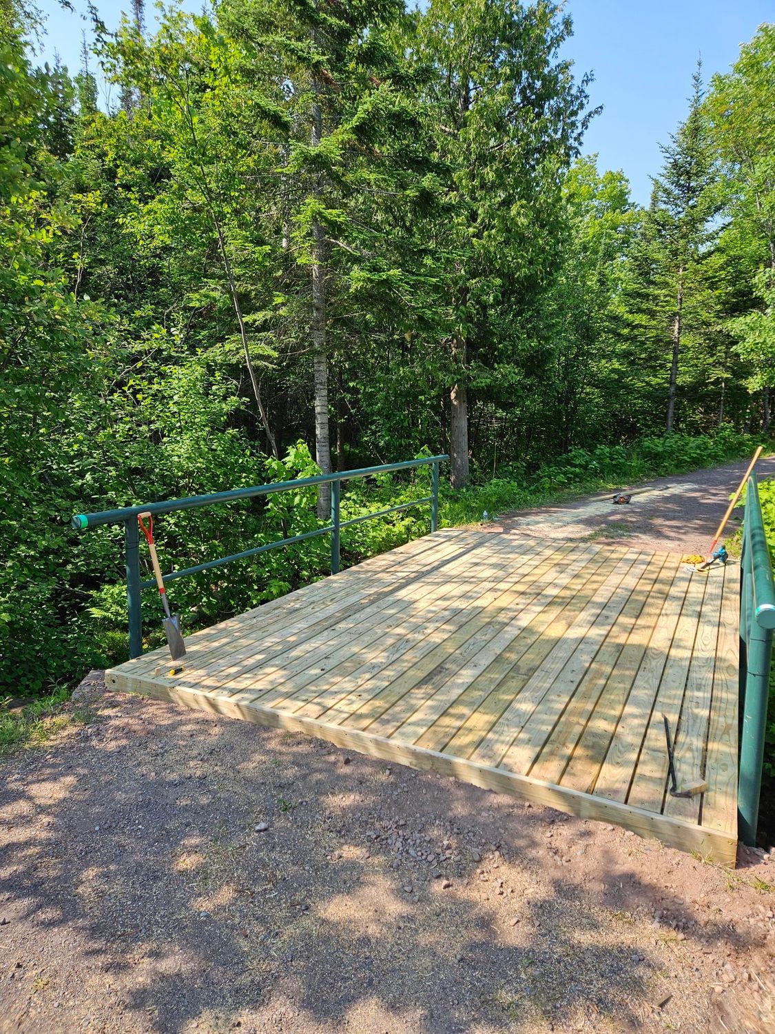 Wooden bridge over a dirt path in a sunny green forest.
