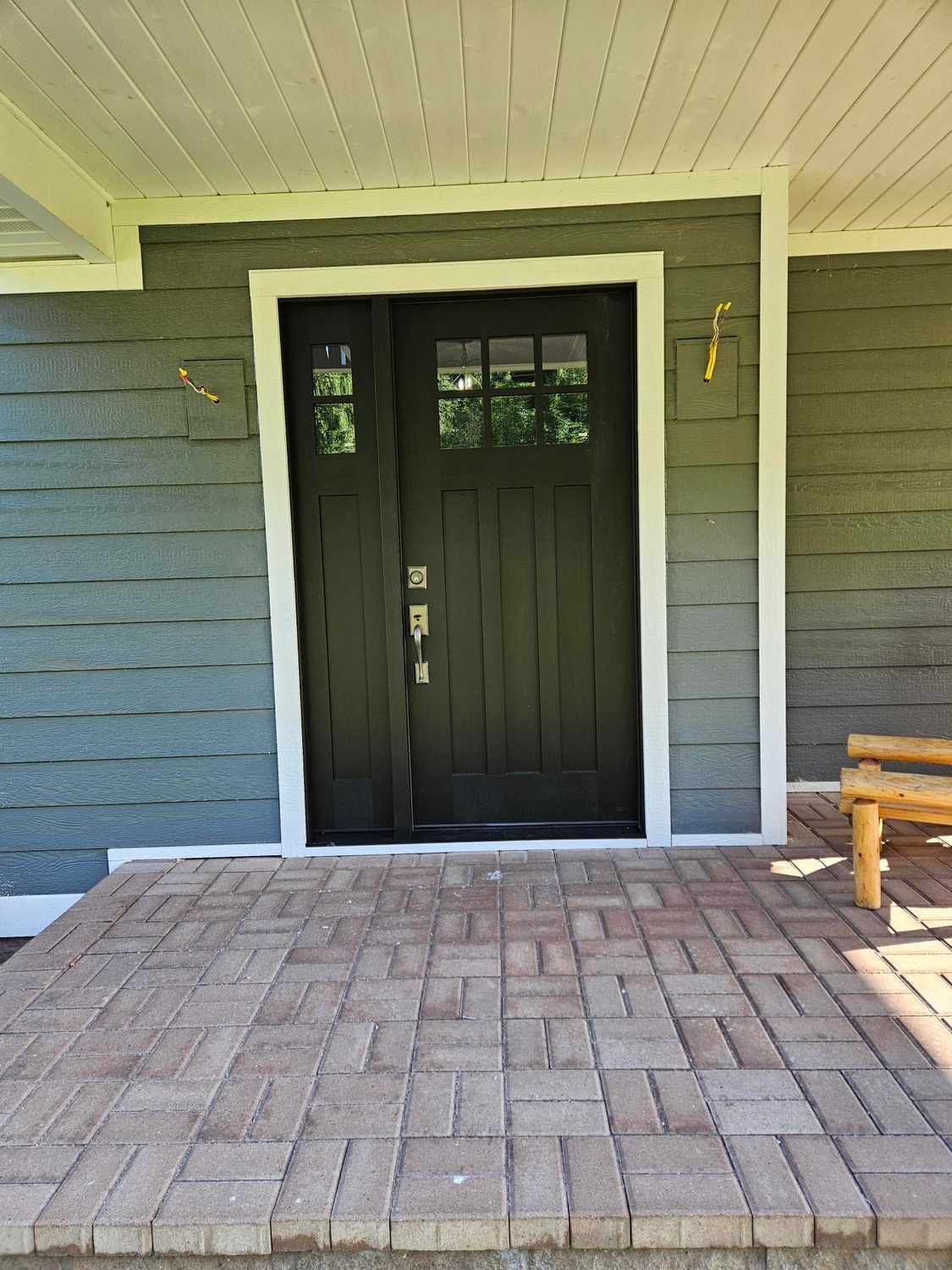 Dark front porch with black double doors, white trim, gray siding, and brick pavers.