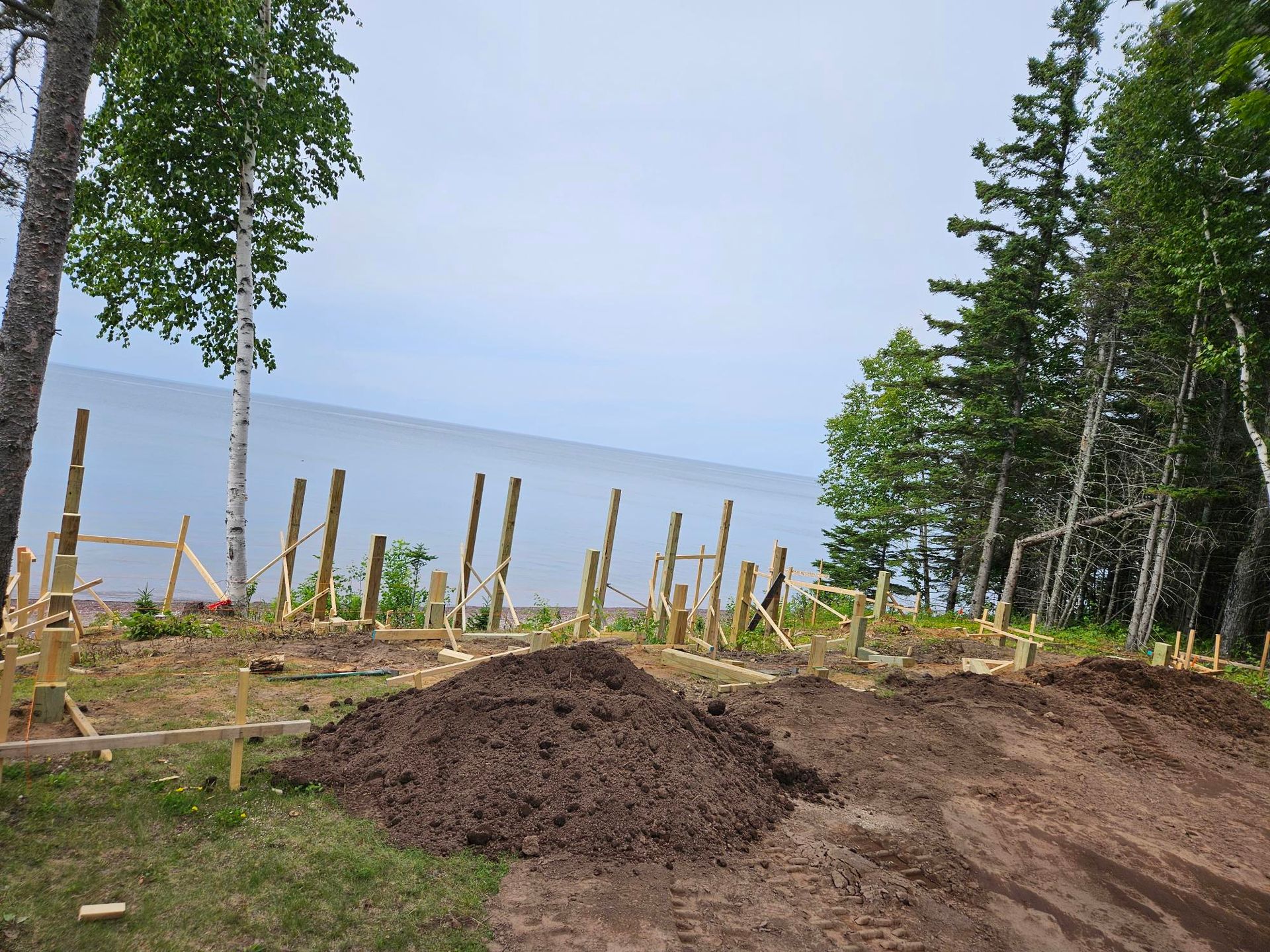 Dirt mound and wooden stakes on a lakeside construction site beside tall trees
