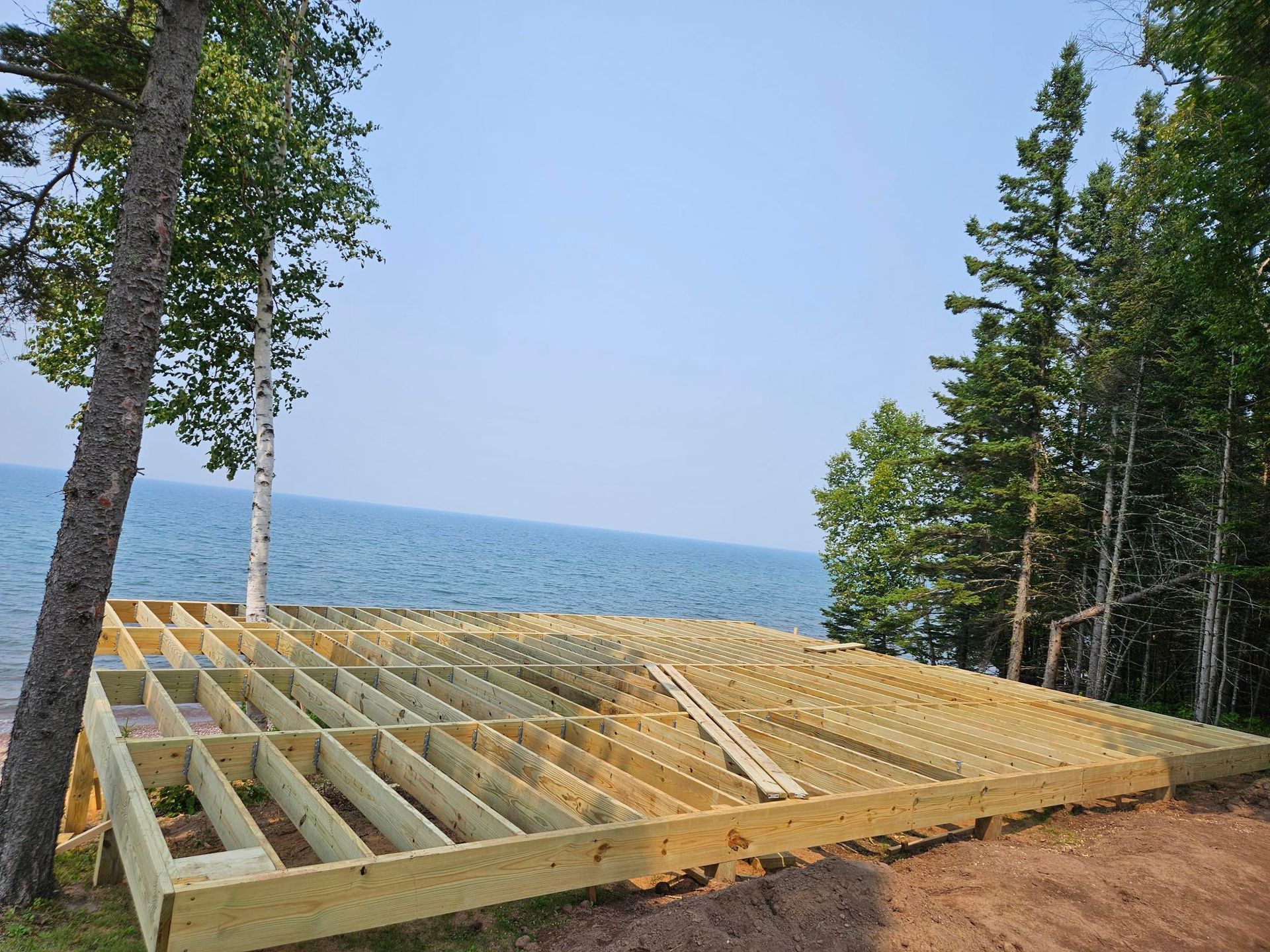 Wooden deck framing beside a lake, with trees and blue water in the background.