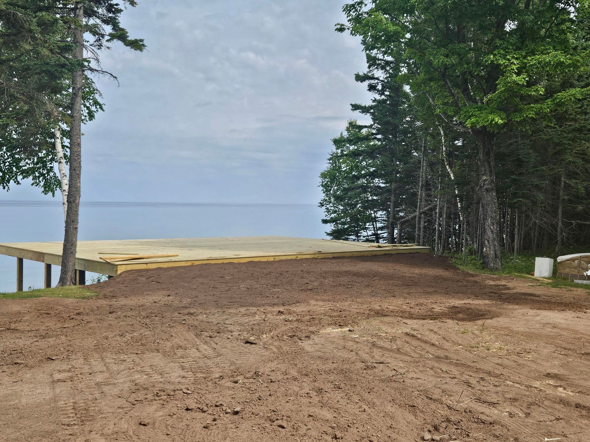 Dirt clearing at a wooded lakeshore with calm water and a cloudy sky