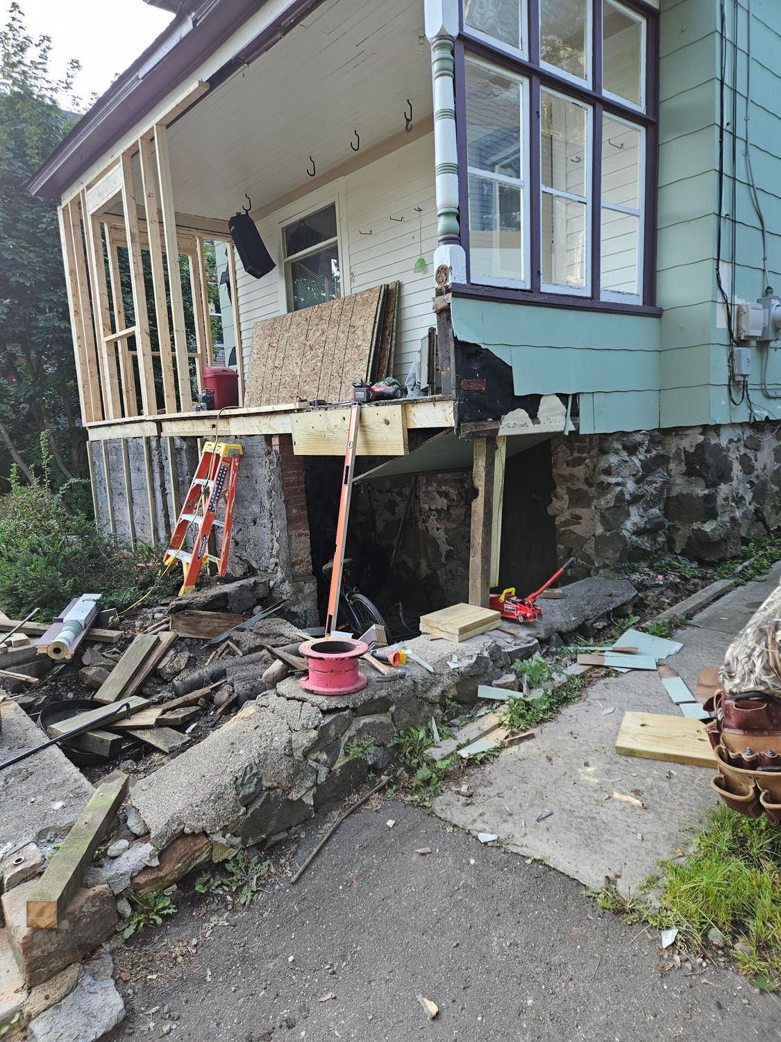 Collapsed porch on a damaged house, with broken steps, debris, and a red ladder underneath