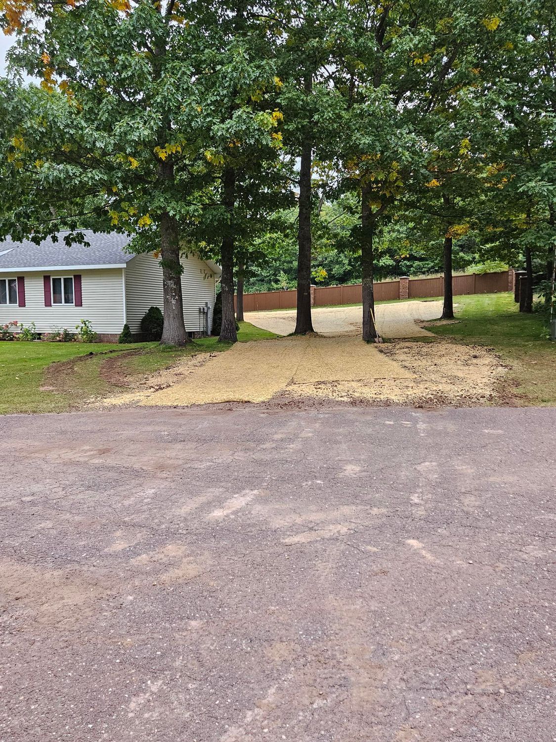 Gravel driveway beside a white house with trees and a wooded yard.