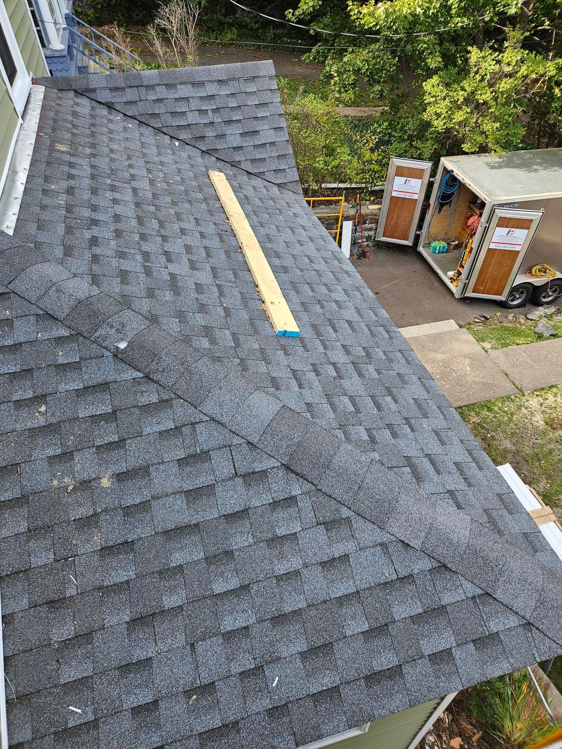 Roof shingles with a long yellow board laid across the slope, viewed from above.