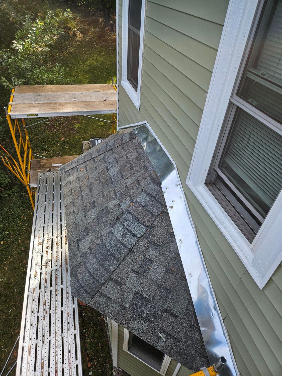 Damaged shingled roof with a large hole beside a house window and gutter.