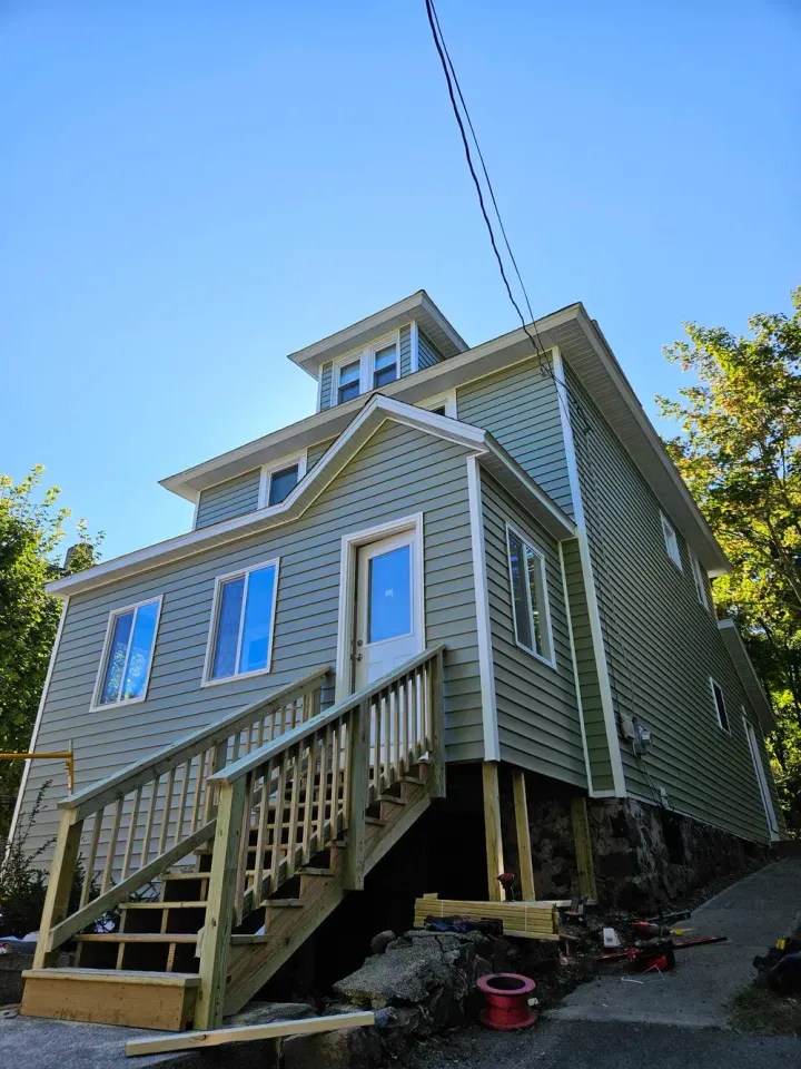 A green house with wooden stairs and porch viewed from below against a blue sky.